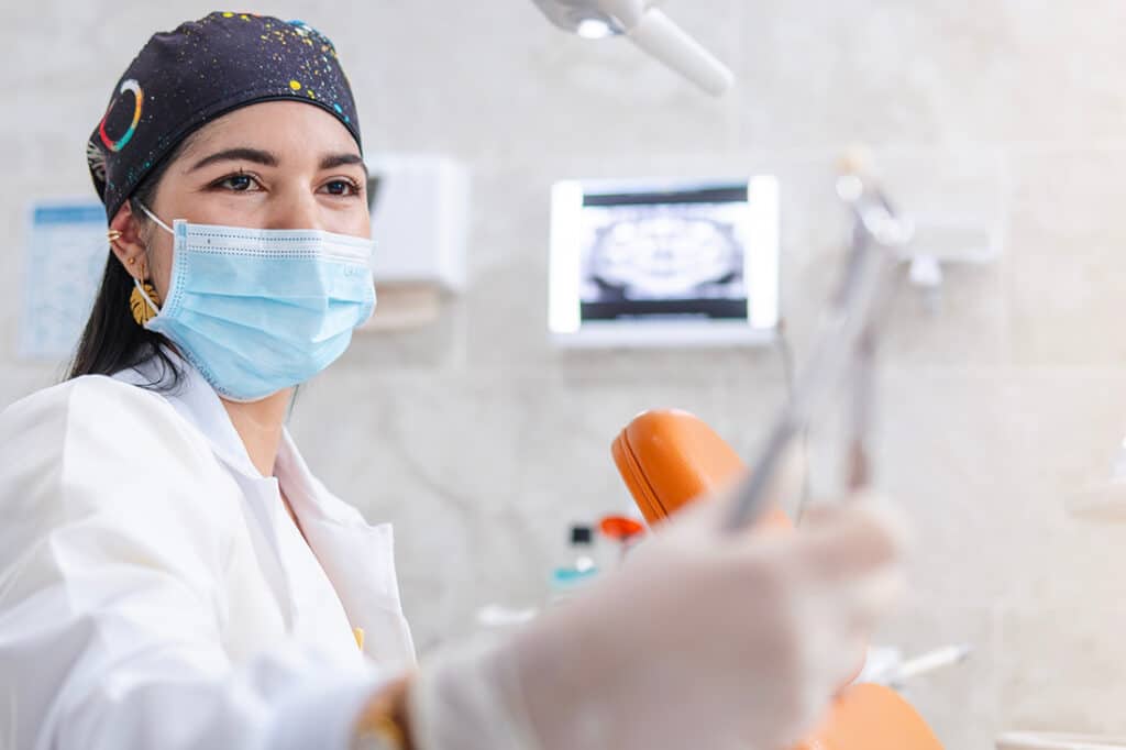 The dentist, specializing in root canal treatments, smiles as she examines a tooth she has removed from a patient and holds it with gripping forceps